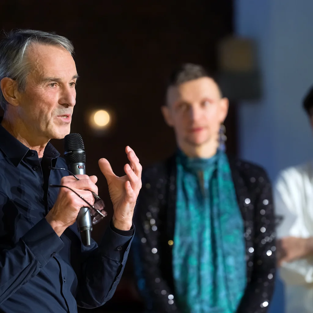Ivo Van Hove spricht in ein Mikrofon, im Hintergrund stehen Tomasz Prasqual und Deniz Bolat.