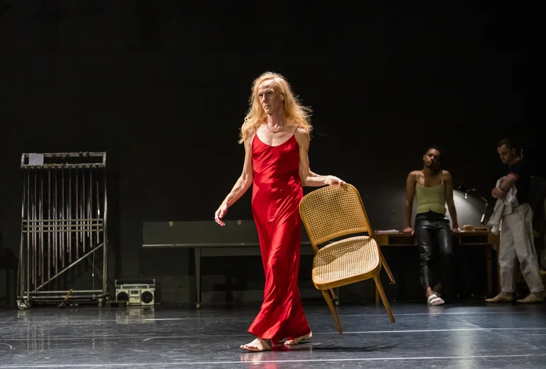 Stage actor in red dress carries chair