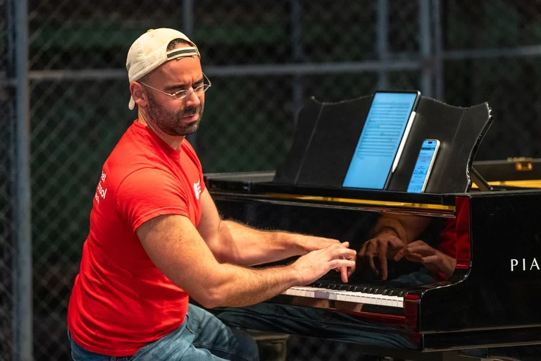 A musician from the group ‘Wild Up’ is playing the piano. He is wearing a red shirt and a cap and is leaning away from the piano with his eyes closed
