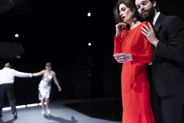 Ein intensiver Moment auf der Bühne: Eine Frau in rotem Kleid wird von einem Mann in schwarzem Anzug gehalten, während im Hintergrund ein weiteres Tanzpaar sichtbar ist.
