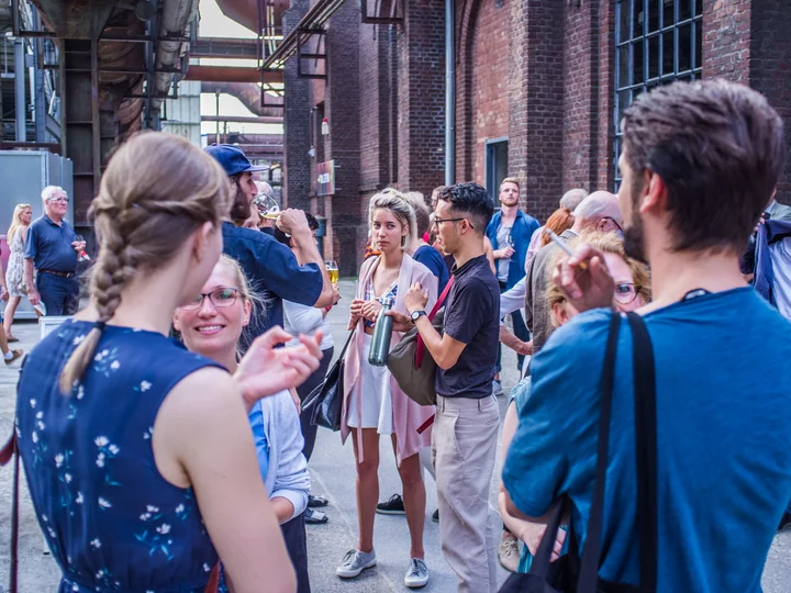 Die Mitglieder des Club.Ruhr unterhalten sich in einer urbanen Industriekulisse mit Backsteinfassaden im Landschaftspark Duisburg-Nord.