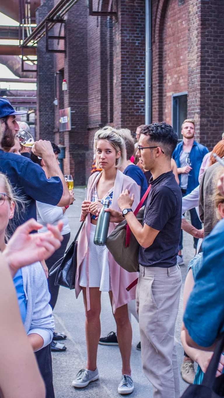 Die Mitglieder des Club.Ruhr unterhalten sich in einer urbanen Industriekulisse mit Backsteinfassaden im Landschaftspark Duisburg-Nord.