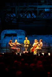 Caroline Shaw singt mit dem Attacca Quartet vor blau beleuchteter Industriekulisse und großem Publikum.