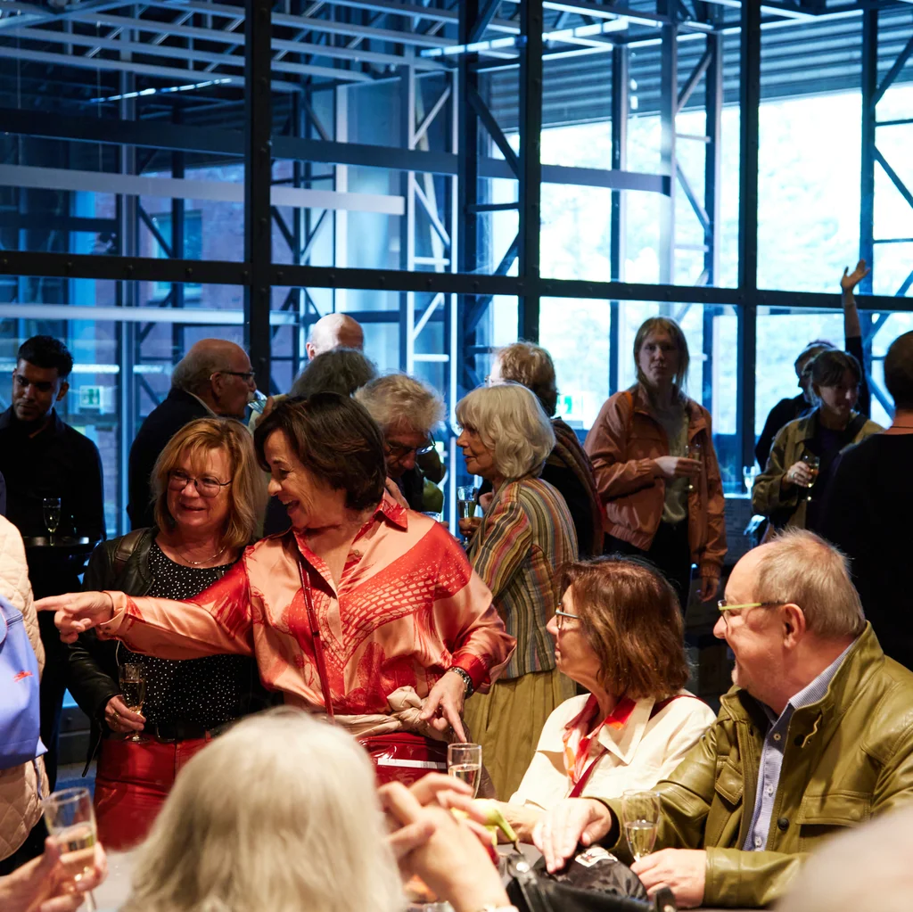 Im Theaterfoyer sitzen und stehen mehrere Menschen und sind im Gespräch miteinander.