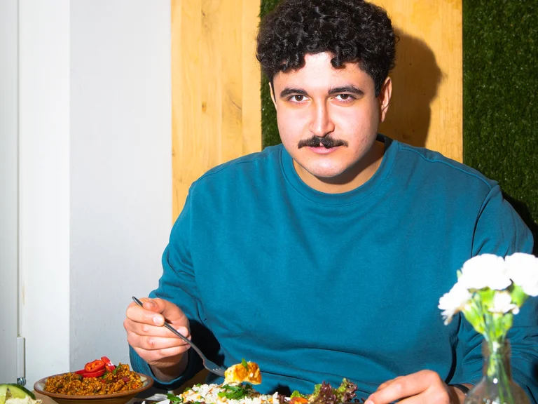 Dein Couseng sits at a table with food and looks at the camera.