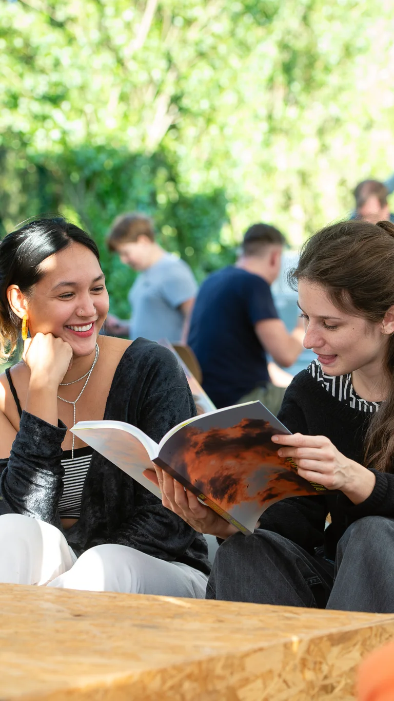 Zwei Besucherinnen, die auf Sitzsäcken sitzen und eine Programmbroschüre der Ruhrtriennale lesen.