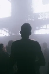 Die Silhouette einer Person inmitten einer tanzenden Menge vor flackernden LED-Flächen.