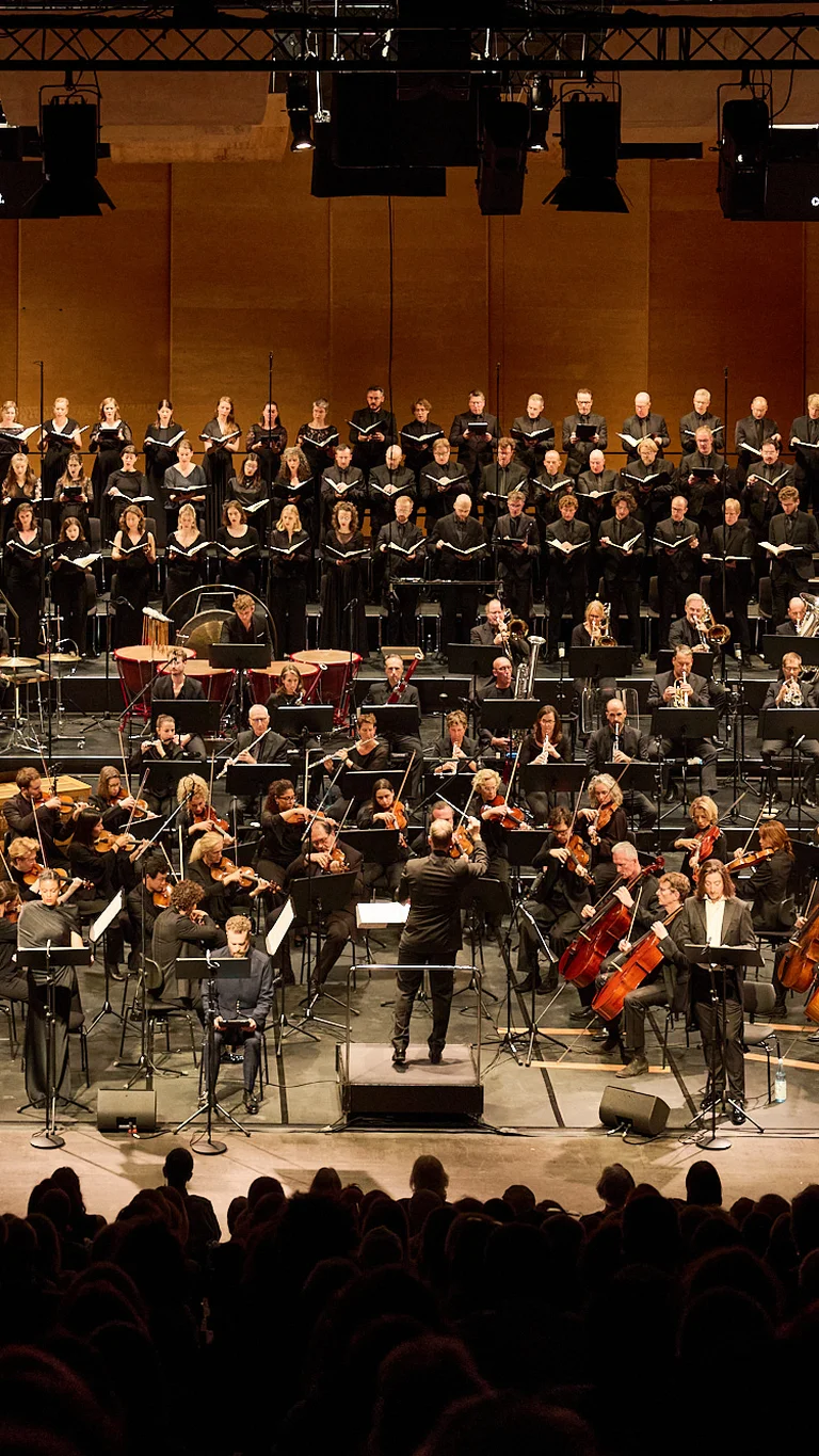 Chorwerk Ruhr und die Bochumer Symphoniker in einem Aufführungsort, im Vordergrund Publikum.