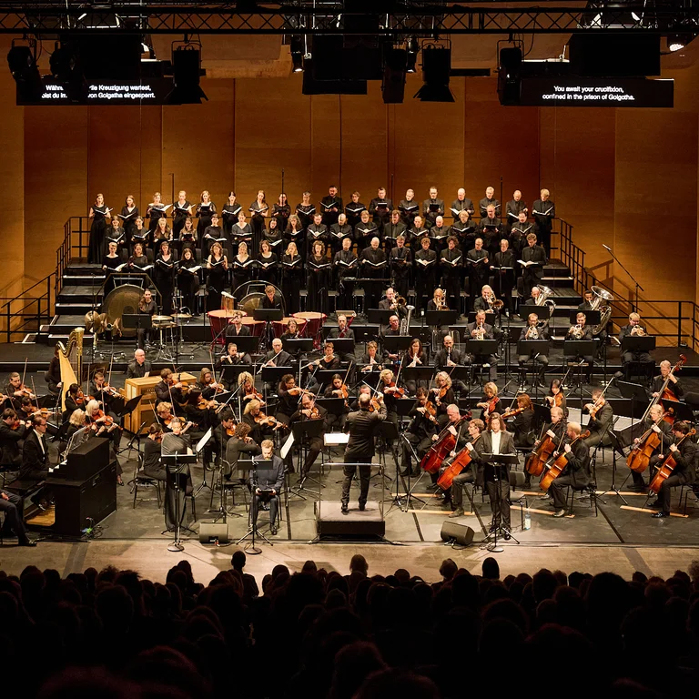 Chorwerk Ruhr and the Bochum Symphony Orchestra at a performance venue, with the audience in the foreground.