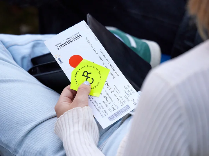 A person is holding an event ticket on their lap.