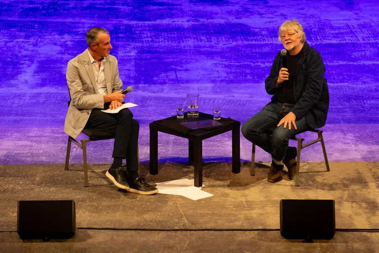 Ivo Van Hove and Will Gregory sitting on stage and speaking into microphones.