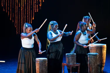 Vier Performerinnen spielen mit erhobenen Trommelstöcken auf großen Trommeln.