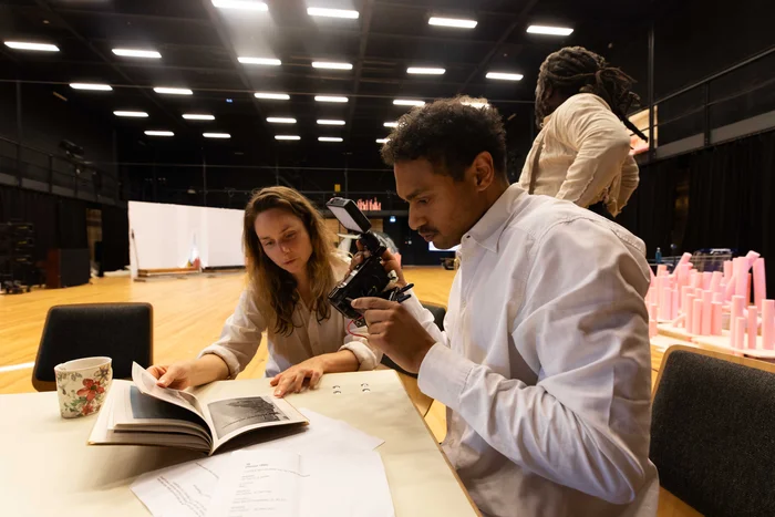 Zwei Personen betrachten gemeinsam ein aufgeschlagenes Buch, das eine der Personen abfilmt.