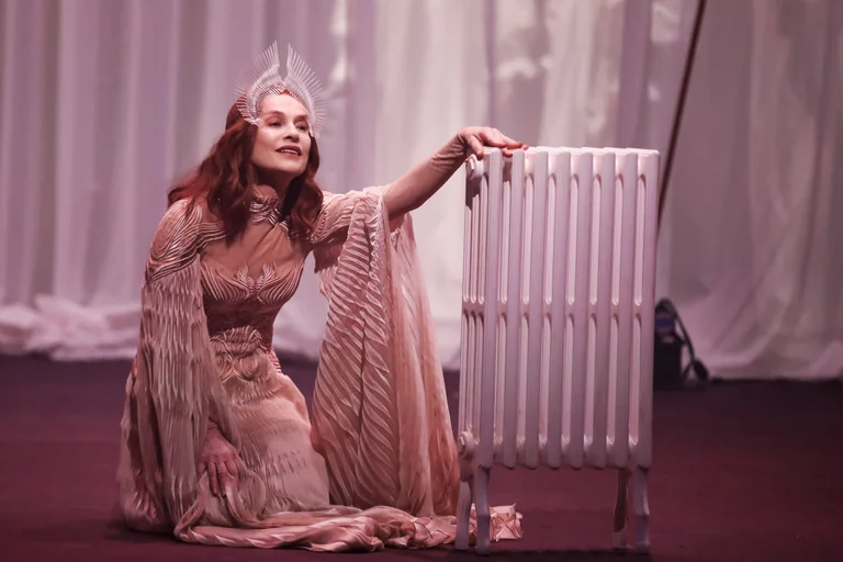 Woman in a dress, the actress Isabelle Huppert, sitting next to a radiator