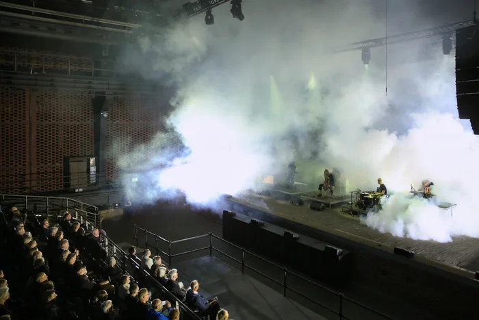 View of the audience and the stage where Rully Shabara, Hildur Guðnadóttir, Sam Slater, and James Ginzburg are performing. Dense clouds of fog fill the space, creating a dramatic atmosphere.