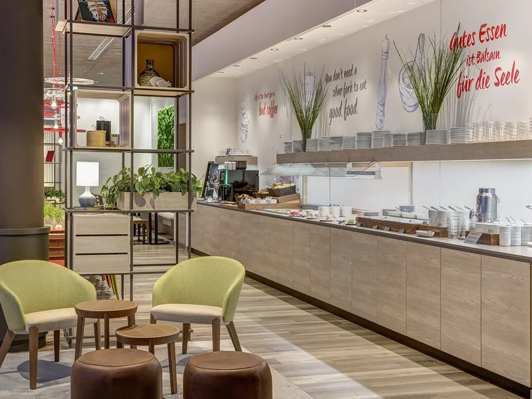 Modern breakfast and lobby area at the Intercity Hotel Duisburg, featuring a buffet, seating areas, and wall lettering.