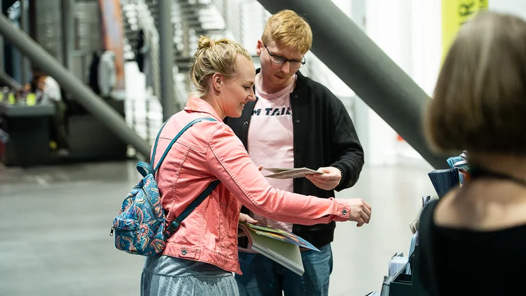 Two people are standing in the foyer of the Jahrhunderthalle Bochum looking at a flyer for the Ruhrtriennale.