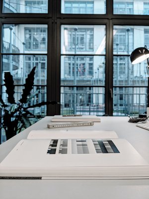 Ryoji Ikedas "continuum" liegt aufgeschlagen auf einem Tisch, eine große Fensterfront ist im Hintergrund zu sehen.
