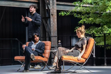 Blick auf die Bühne bei der Diskursveranstaltung "Brave New Voices" mit Autorin und Dramatikerin Sivan Ben Yshai und Moderatorin Fatima Khan. Im Hintergrund steht der Dolmetscher Lars Grombelka und übersetzt das Gespräch in Deutsche Gebärdensprache.