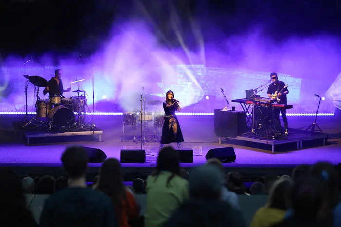 Gaye Su Akyol performs with her band on stage in purple light and haze in front of an audience.