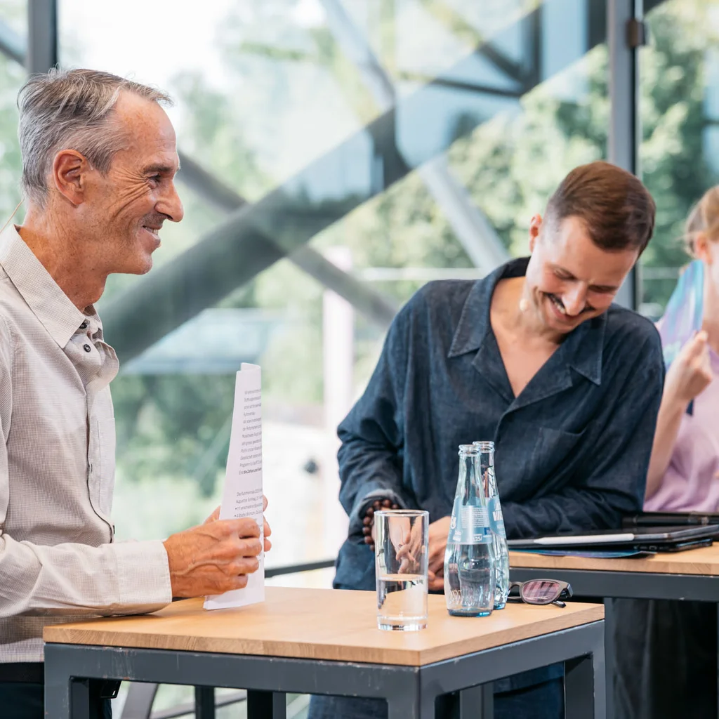 Ruhrtriennale-Intendant Ivo Van Hove, Programmdirektor Krystian Lada und Britta Schünemann, Leitende Dramaturgin der Ruhrtriennale, stehen nebeneinander an Stehtischen im oberen, verglasten Foyer der Jahrhunderthalle Bochum. Die Stimmung ist ausgelassen.