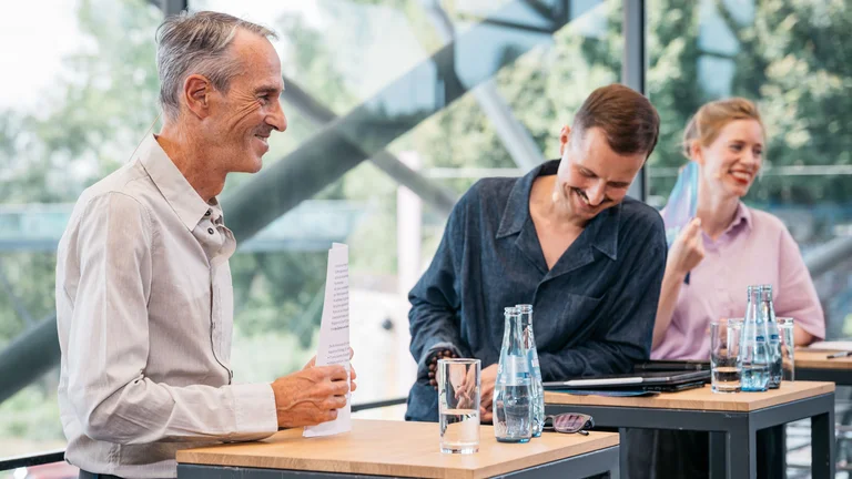 Ruhrtriennale-Intendant Ivo Van Hove, Programmdirektor Krystian Lada und Britta Schünemann, Leitende Dramaturgin der Ruhrtriennale, stehen nebeneinander an Stehtischen im oberen, verglasten Foyer der Jahrhunderthalle Bochum. Die Stimmung ist ausgelassen.