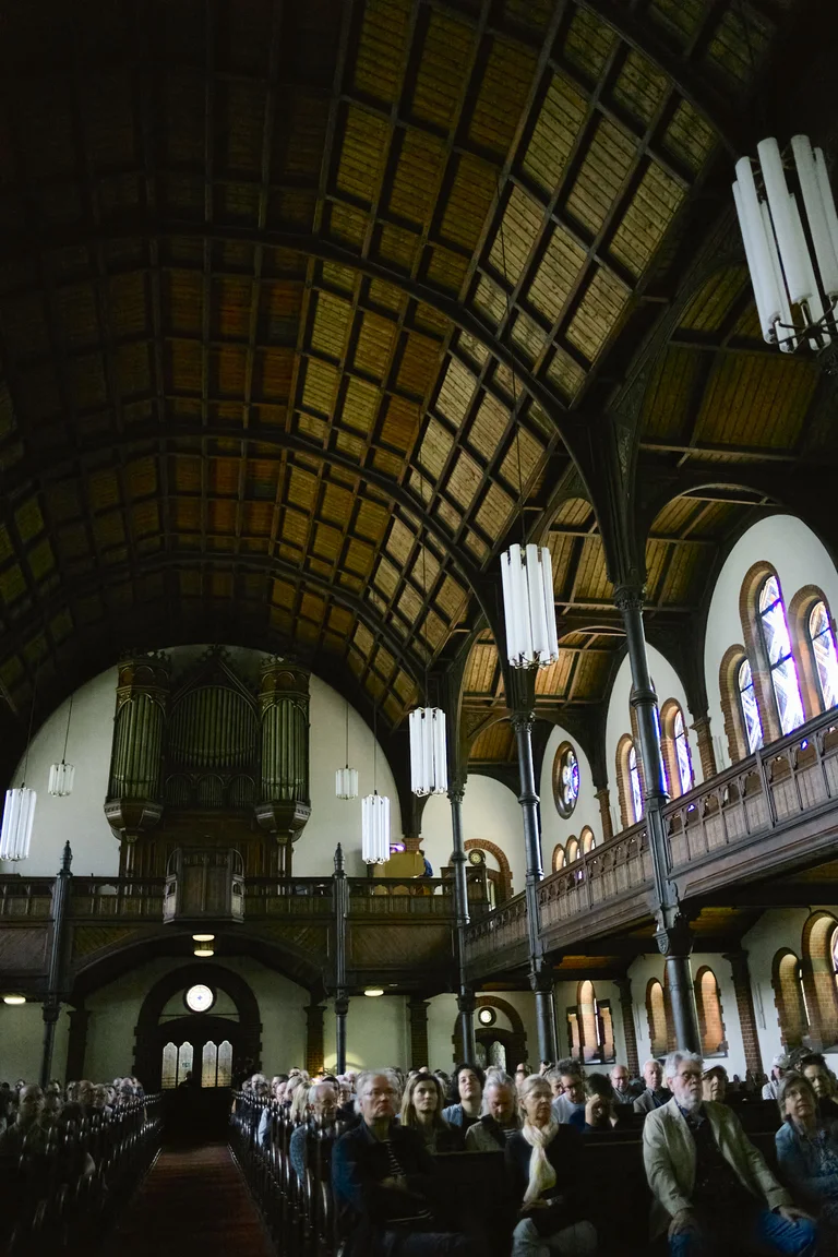 View inside the Evangelical Church at the Market in Katernberg during the event 124 Years of Reverb. The tall wooden barrel-vaulted ceiling and balconies dominate the space, with the large church organ rising at the back. The pews are filled with many attendees, while soft light filters through the stained-glass windows.
