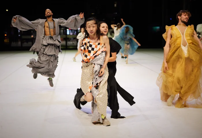 MehrereTänzer:innen der Dresden Frankfurt Dance Company stehen in bunten Kostümen auf einer Bühne.um.