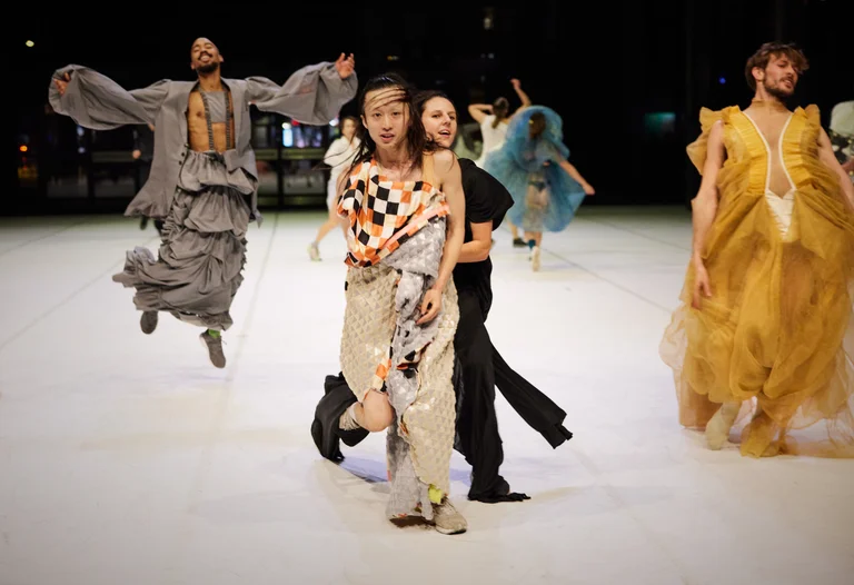 MehrereTänzer:innen der Dresden Frankfurt Dance Company stehen in bunten Kostümen auf einer Bühne.um.