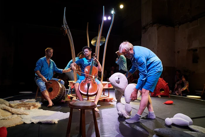 Die Gruppedas Ensemble des belgischen Theater "De Spiegel" führt "AORTA" mit ihren Instrumenten und Handpuppen in der Mitte der Bühne auf. Kinder sitzen im Kreis um sie herum. Die Musiker musizieren