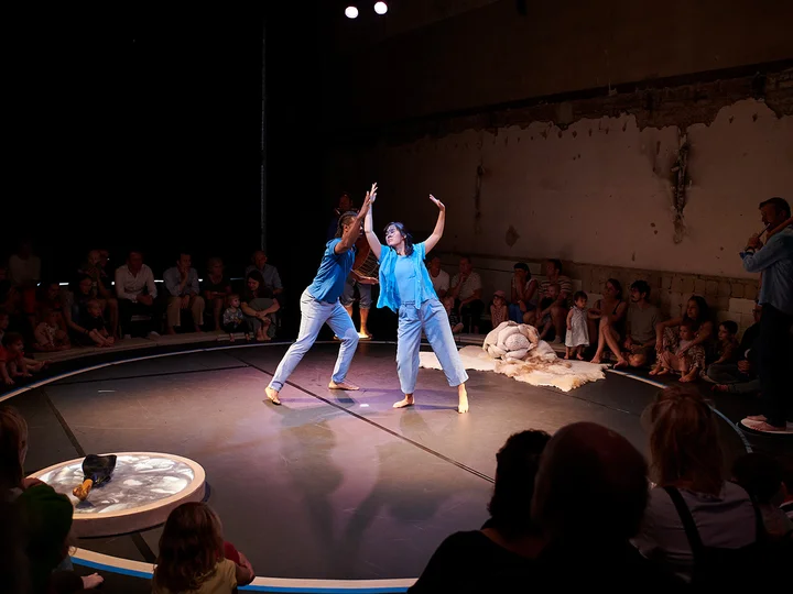 Two dancers from the ensemble in the centre of the stage. The light is directed at them. The piece ‘Little Ears, Tiny Feet’ is performed at the Dampfgebläsehaus in Bochum