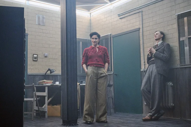 Two actors in retro clothing inside a stage set designed as a simple office.
