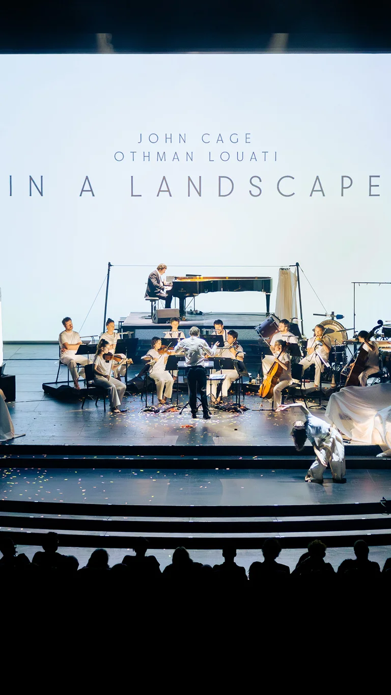 Das Ensemble Les Apaches ! spielt auf einer hell ausgeleuchteten Bühne vor der Projektion „In a Landscape“.