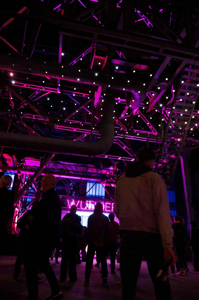 Menschen tanzen unter einem lila beleuchteten Industriedach. Im Hintergrund kann man das Wort "Wunder" über der DJ Booth lesen.