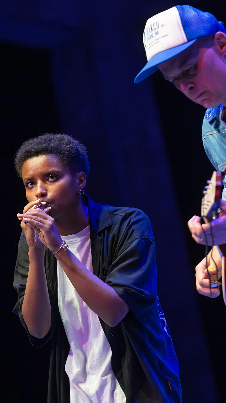 Meskerem Mees spielt Mundharmonika am Mikrofon, während neben ihr Carlos Garbin Gitarre spielt.