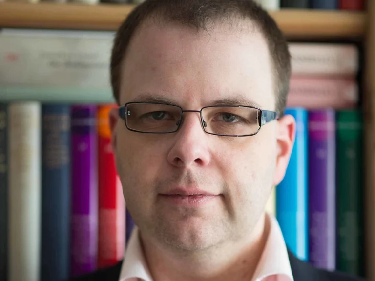 Sascha Westphal looks into the camera in front of a bookshelf.