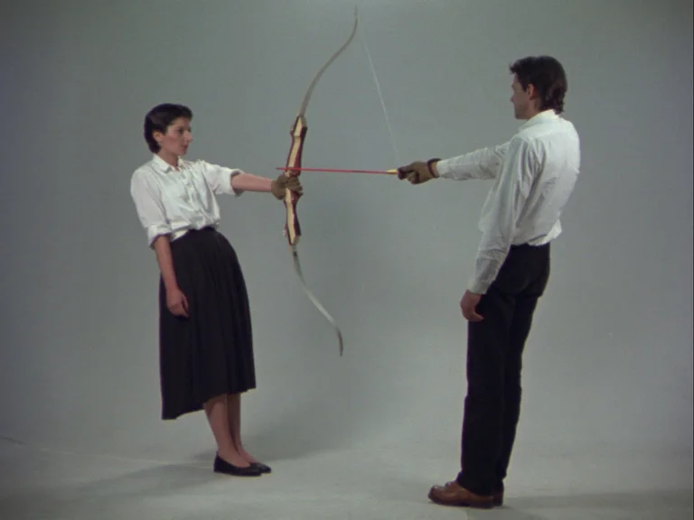 Marina Abramović and Ulay stand facing each other; Ulay holds the bow with the string drawn, the arrow aimed at Marina Abramović.