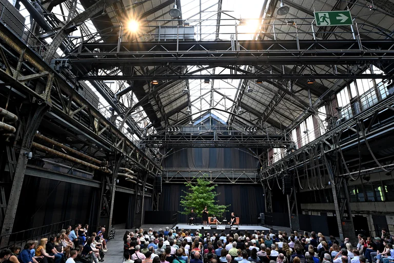 A wide-angle shot of the format ‘Barve New Voices’ in the Jahrhunderthalle, Bochum. The audience can be seen as Edouard Louis on the stage in the talk