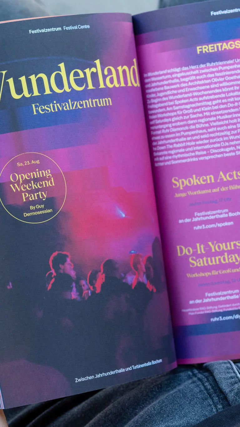 A person holds an open Ruhrtriennale festival program displaying brightly designed pages with information about the Wunderland festival centre.