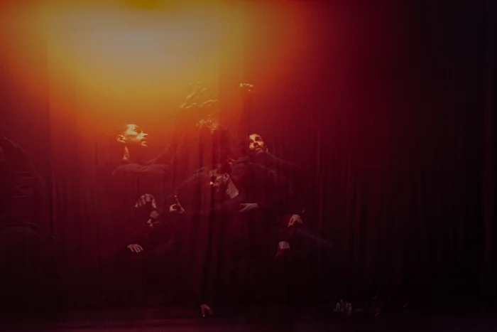 Multiple-exposure image captures layered movements of Mohamed Toukabri in a reddish-yellow light atmosphere. Gestures and facial expressions blur into the color gradient.