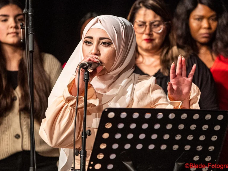 A young woman with a microphone in front of a music stand, with other people behind her.