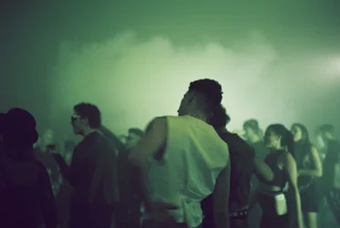 Menschen tanzen dicht beieinander in einer dunklen, nebeligen Clubatmosphäre mit grünlichem Licht.