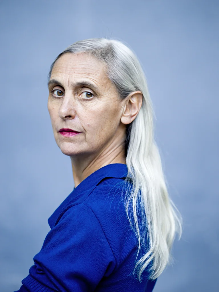 Blonde Frau in blaumen Oberteil, in die Kamera blickend
