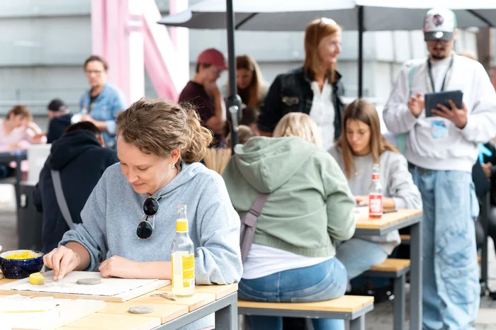Besucher:innen sitzen an Tischen und gestalten kreative Arbeiten.