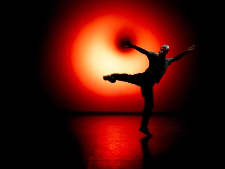 Mohamed Toukabri in Sprungpose vor einem intensiv leuchtenden roten Lichtkreis auf der Bühne.