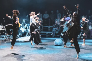 Mehrere Performer:innen tanzen gleichzeitig über die Bühne. Das Publikum umgibt die Spielfläche.