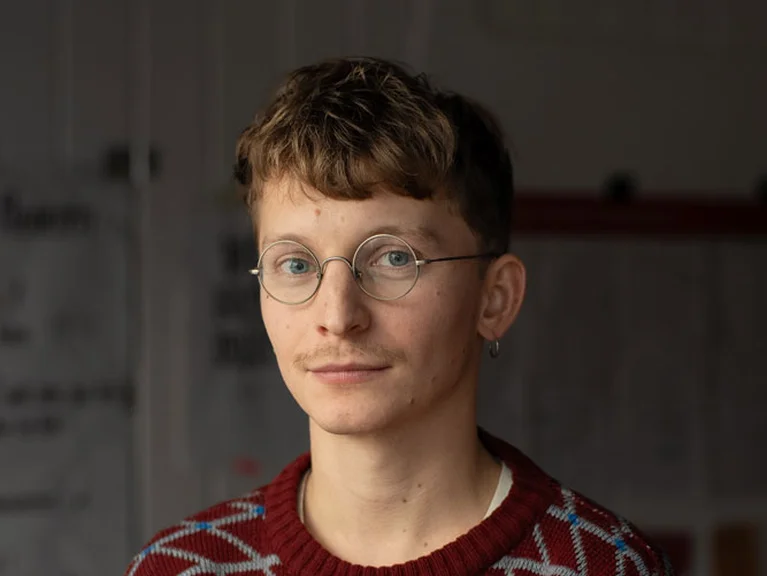 Portrait von Dirk Hornschuch in rot gemustertem Pullover, frontal aufgenommen in einem Innenraum.