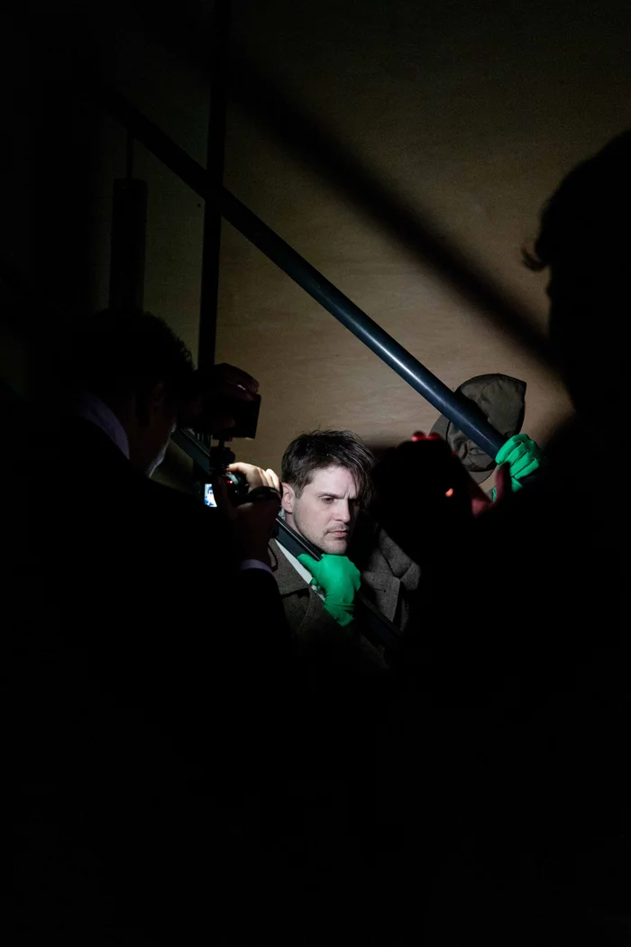 Eine Person steht in einem dunklen Raum auf einer Treppe und wird von mehreren Kameras und Lichtquellen aufgenommen.