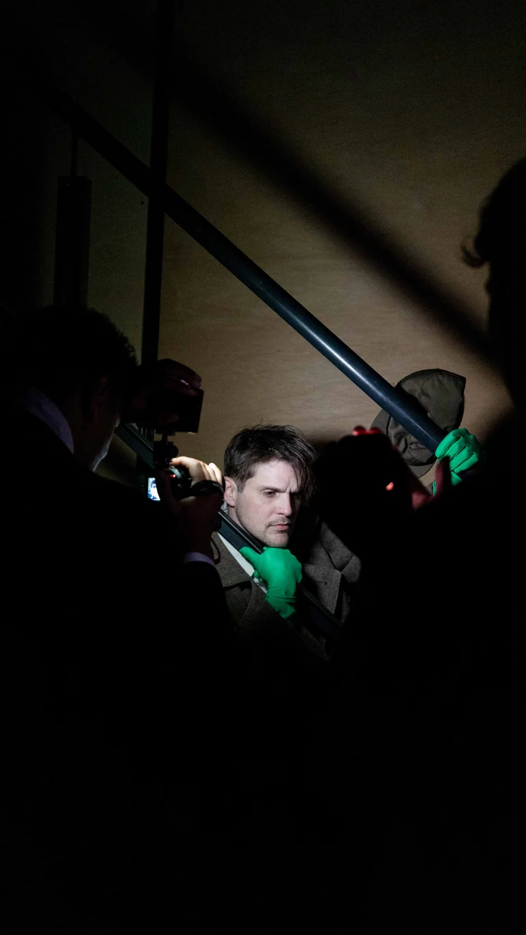 Eine Person steht in einem dunklen Raum auf einer Treppe und wird von mehreren Kameras und Lichtquellen aufgenommen.