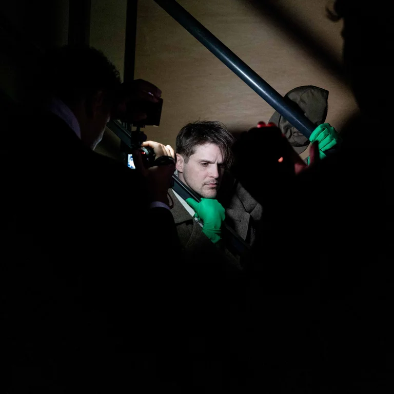 Eine Person steht in einem dunklen Raum auf einer Treppe und wird von mehreren Kameras und Lichtquellen aufgenommen.